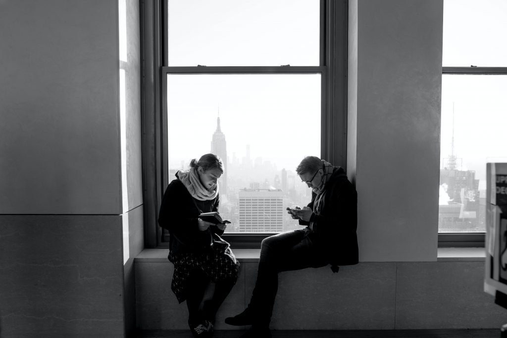 Two people reading while sitting in a windows. Black and white photo.